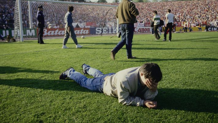 A fan with his hand over his face as he lies face down on the pitch, with other fans walking in the background, during the European Cup Final between Juventus and Liverpool, at the Heysel Stadium in Brussels, Belgium, 29th May 1985. The final saw the Heysel Stadium disaster which resulted in 39 deaths and hundreds of injuries when a retaining wall collapsed at the stadium. (Photo by Bongarts/Getty Images) heysel