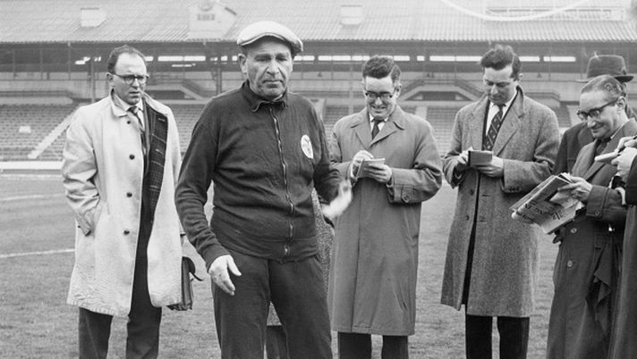 Benfica coach and manager Bela Guttmann (1900 - 1981) with a group of journalists at White City in London, 4th April 1962. He had just accused Tottenham Hotspur of watering the pitch at White Hart Lane, in preparation for their game against Benfica the next day. The match was the second leg semi-final of the European Cup. (Photo by Keystone/Hulton Archive/Getty Images) Bela Guttmann