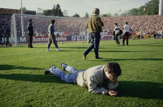 Un tifoso con la mano sul viso mentre giace a faccia in giù sul campo, con altri tifosi che camminano sullo sfondo, durante la finale di Coppa dei Campioni tra Juventus e Liverpool, allo stadio Heysel di Bruxelles, in Belgio, il 29 maggio 1985. La finale fu teatro del disastro dello stadio Heysel, che causò 39 morti e centinaia di feriti a causa del crollo di un muro di contenimento dello stadio. (Foto di Bongarts/Getty Images) heysel
